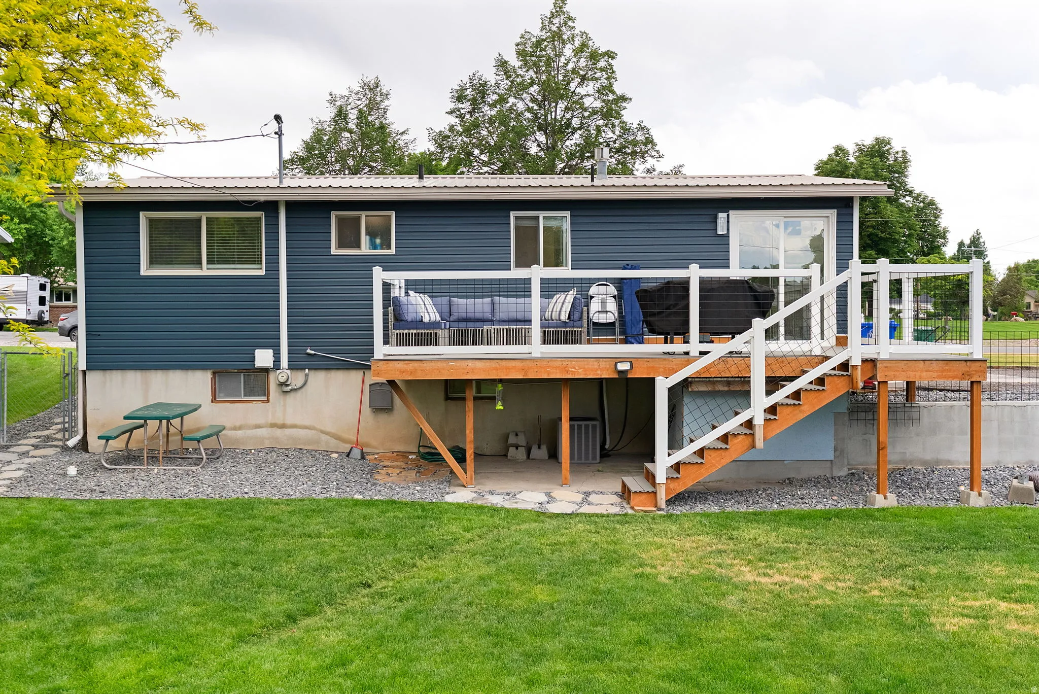Rear exterior featuring a spacious wooden deck with white railings, a sliding glass door, and a manicured lawn