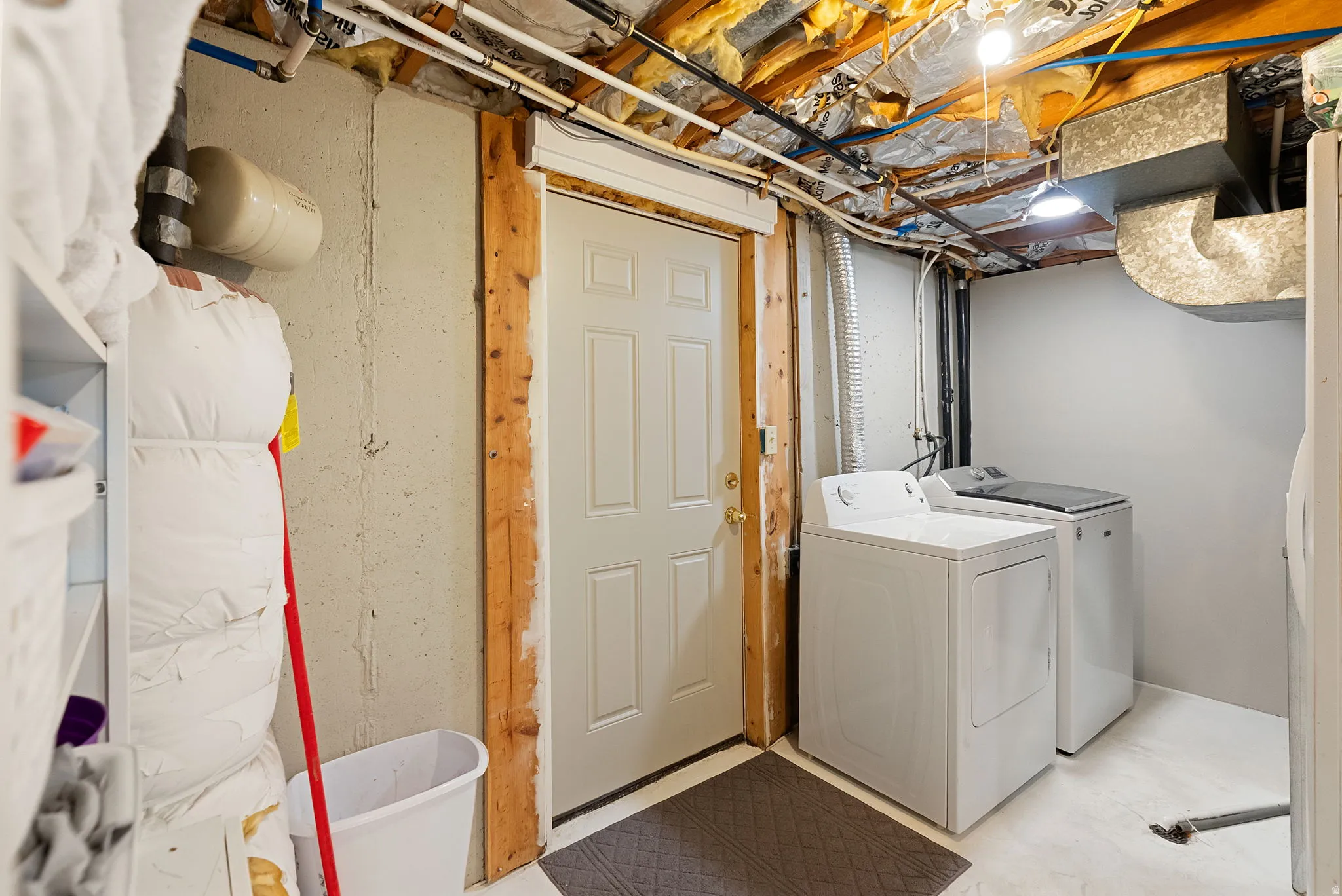 Utility area featuring a white paneled door, exposed ceiling joists, and a washer and dryer set