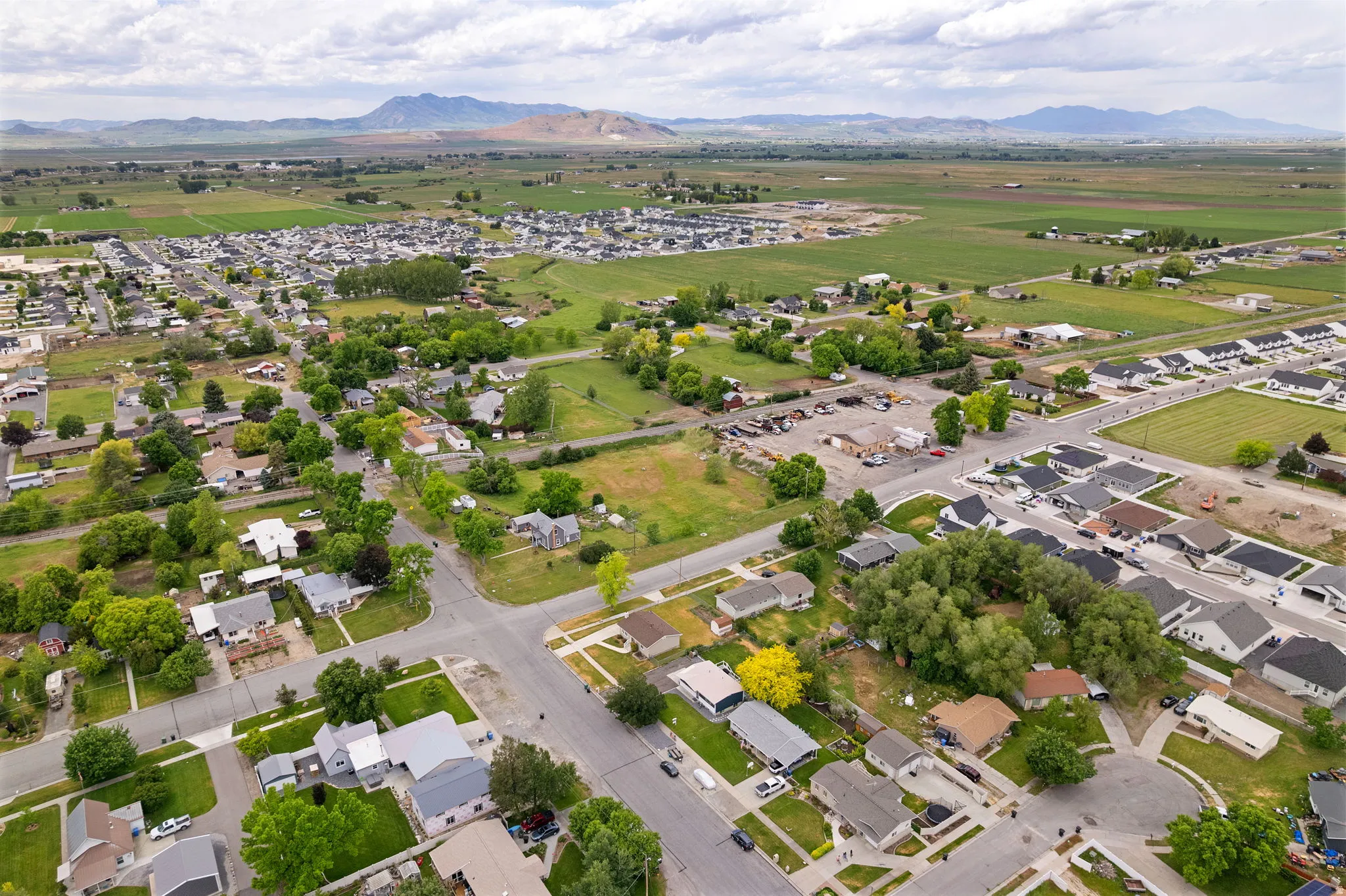 Aerial perspective showcasing a residential community with established homes and new construction, surrounded by open fields and distant mountains