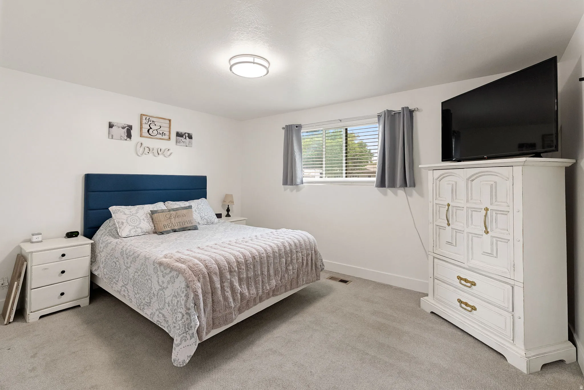 Carpeted room with white walls, a single window featuring horizontal blinds and gray curtains, and a flush-mount ceiling light fixture