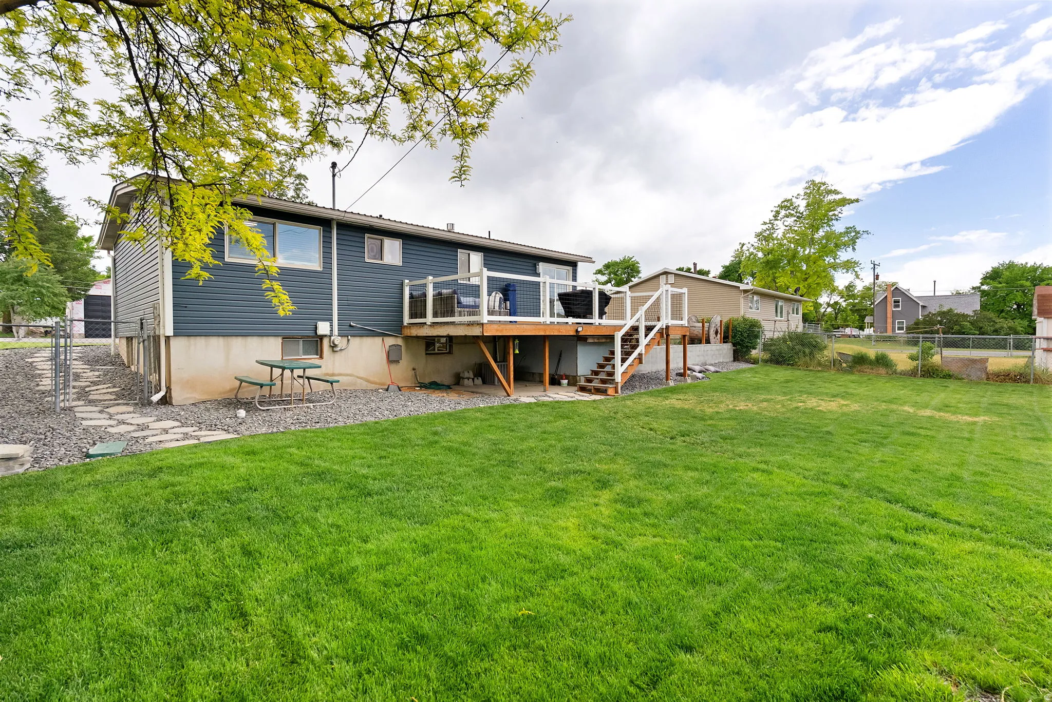Expansive backyard featuring a lush lawn, multi-level deck with glass panel railing, and gravel landscaping