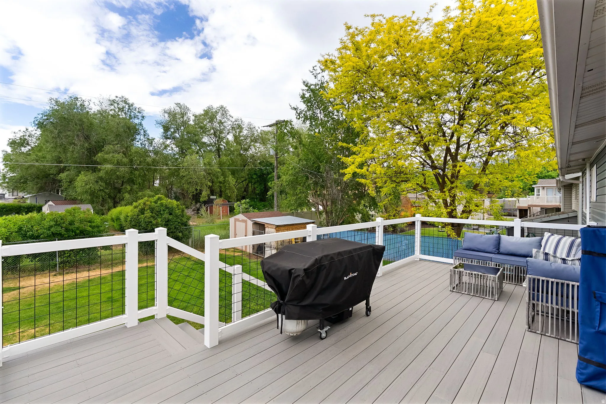 Spacious outdoor deck featuring composite decking, white railing with black wire infill, and a mature tree providing natural shading