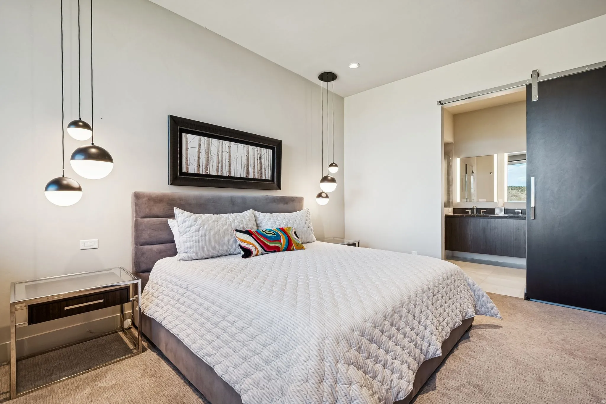Bedroom with a barn door, light colored carpet, ensuite bath, and recessed lighting