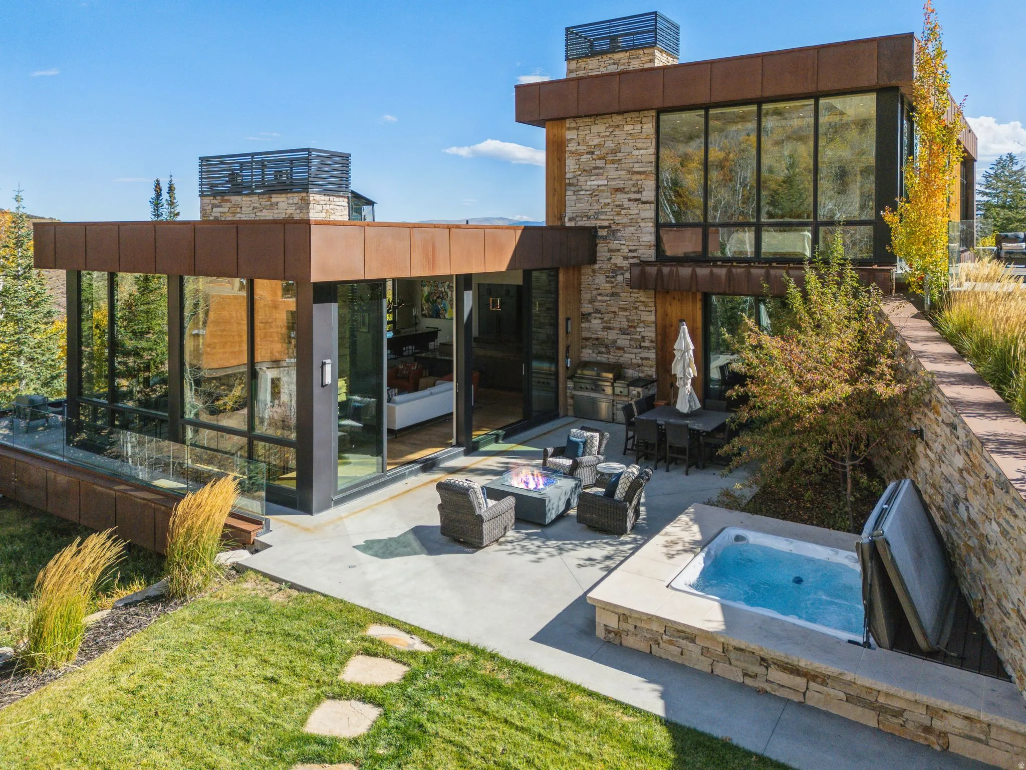 Rear view of house with a fire pit, a patio area, an outdoor hot tub, stone siding, and a sunroom