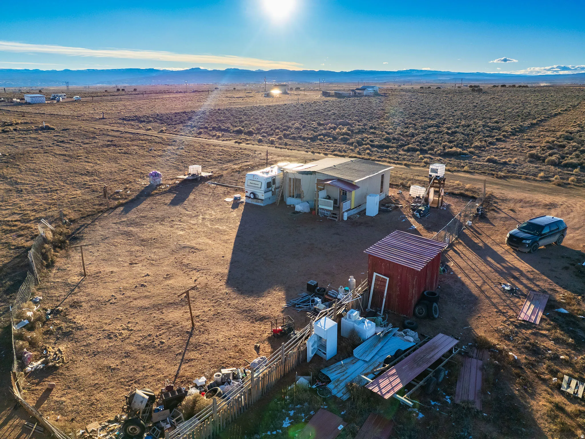 Expansive, undeveloped parcel featuring a single-story structure with a covered porch, an auxiliary red shed with a corrugated metal roof, and a visible water storage system