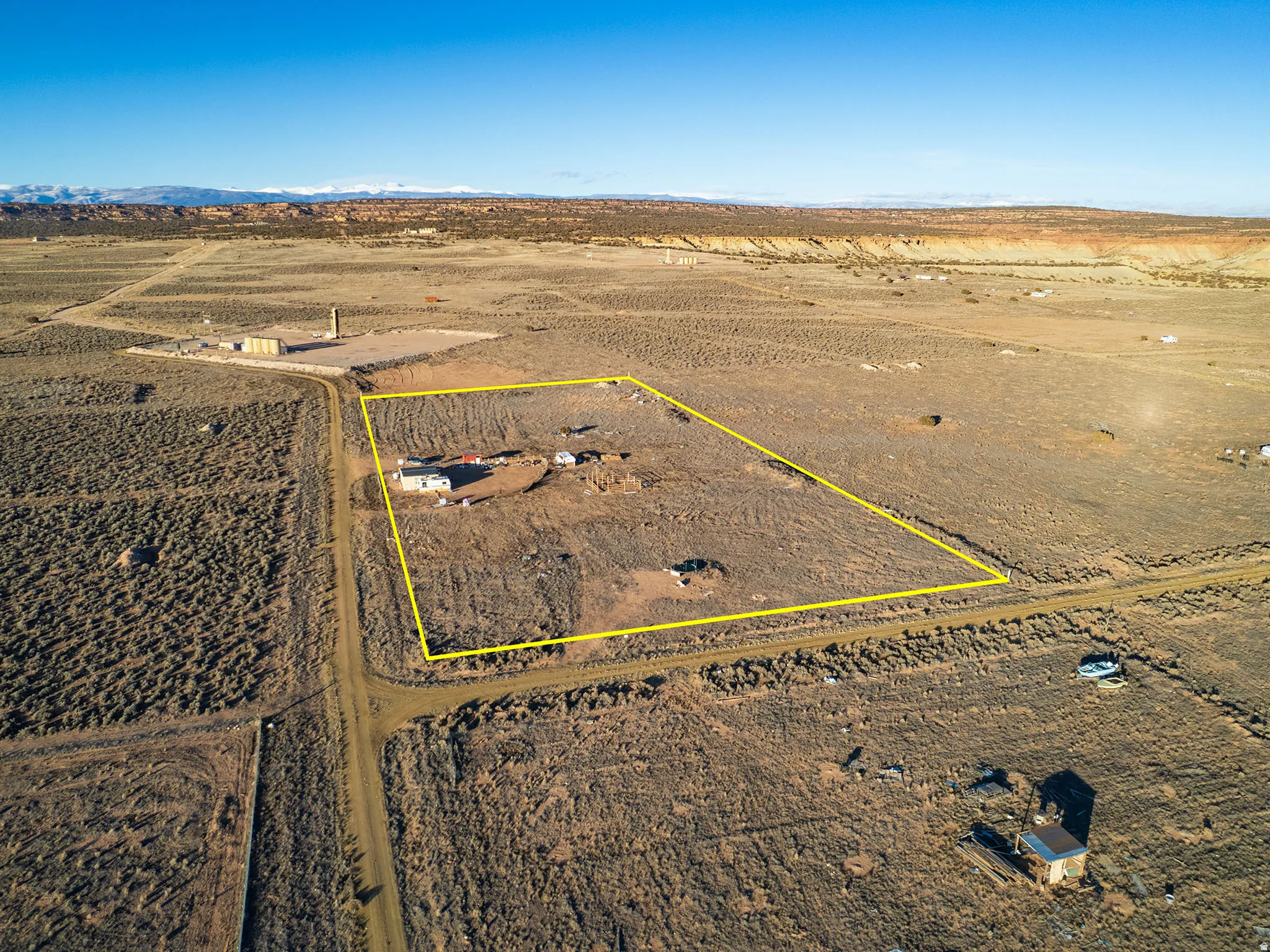 Expansive desert property featuring a single-story dwelling, a surrounding dirt road, and visible mountain ranges