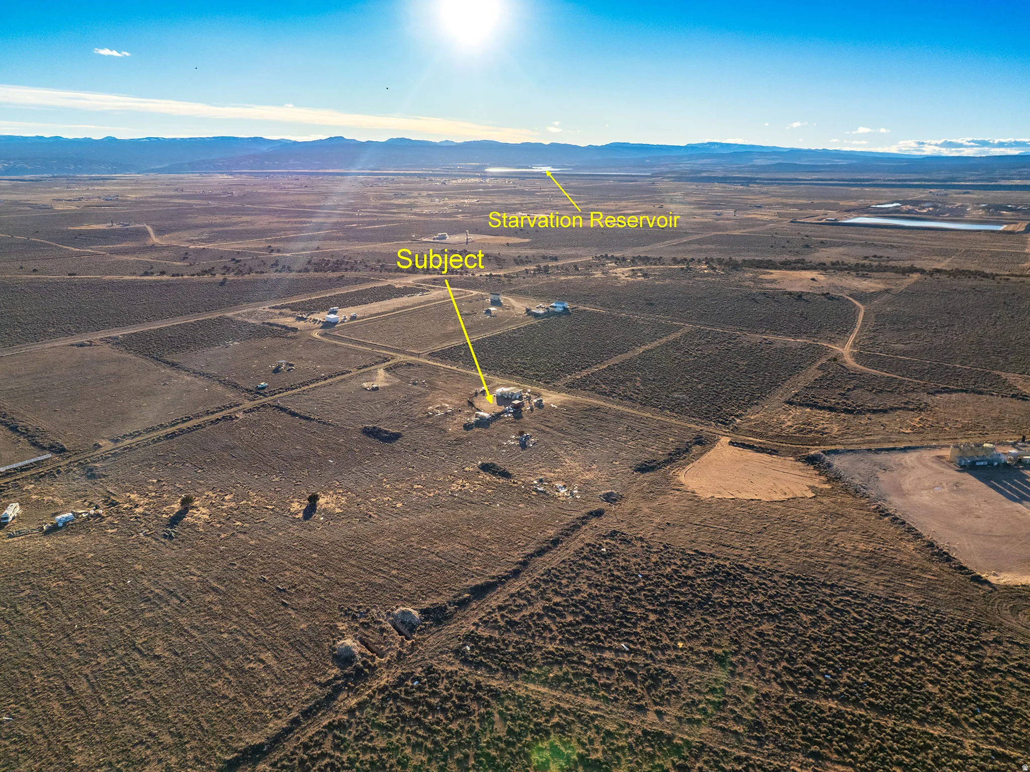 Expansive aerial perspective showcasing a significant land parcel with distant mountain ranges and a visible reservoir