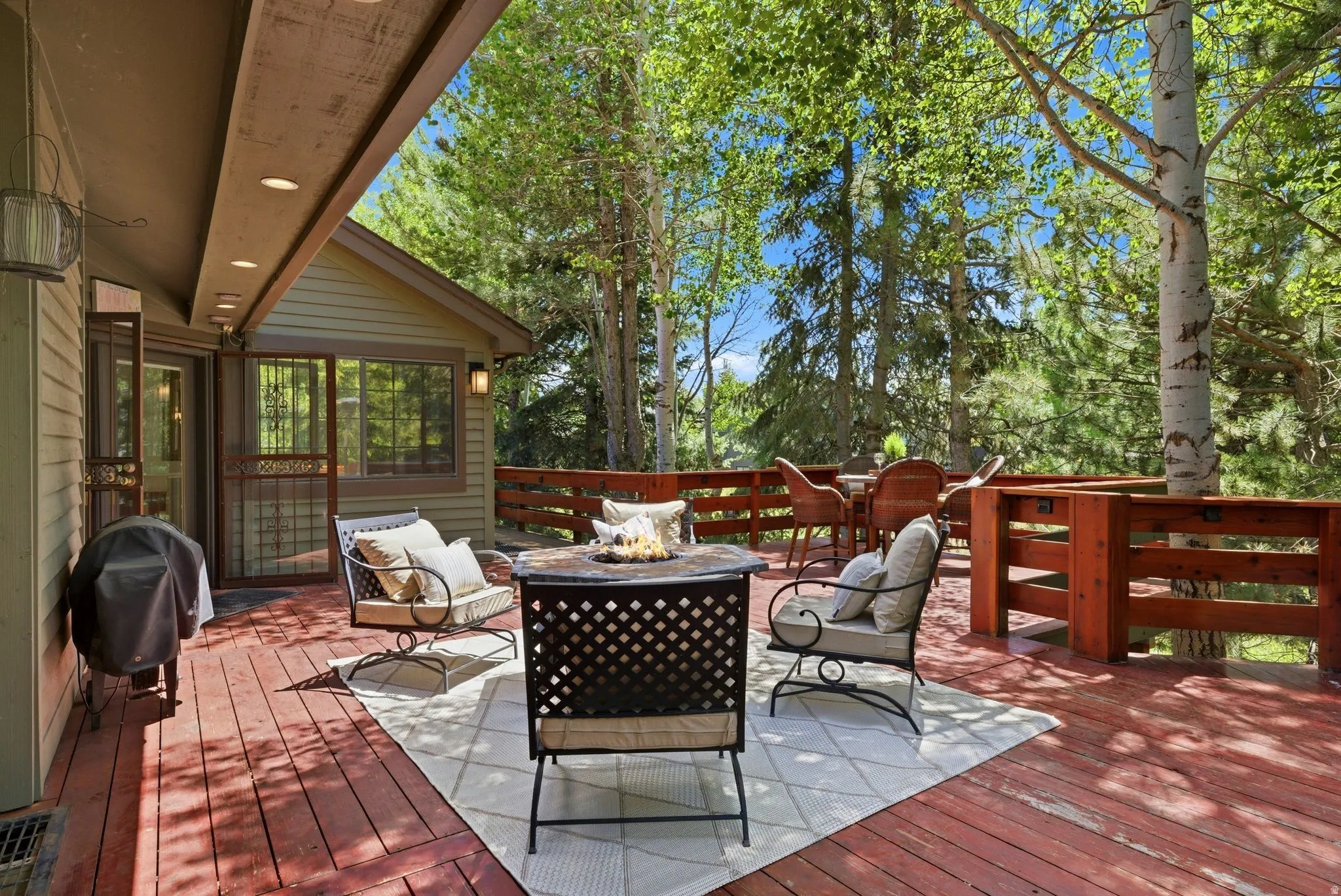 Expansive red-stained wood deck featuring a built-in railing system, recessed soffit lighting, and direct access to the interior through a glass-paneled door with an ornamental screen