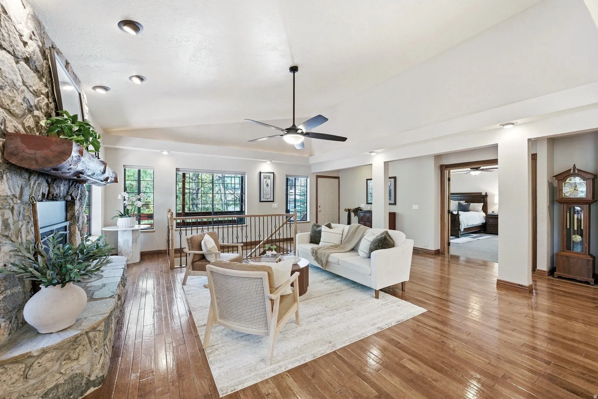 Spacious living area featuring wood-finish flooring, a stone-clad fireplace with a hearth, recessed lighting, and a ceiling fan