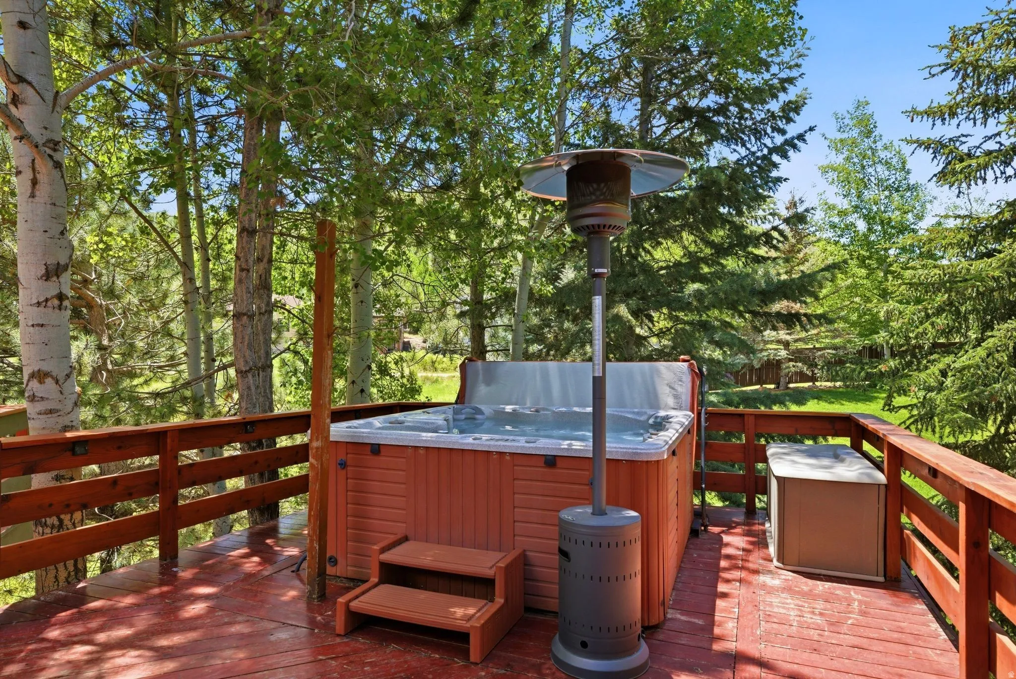 Spacious wooden deck featuring an integrated hot tub with accompanying steps, a protective railing, and surrounding mature trees