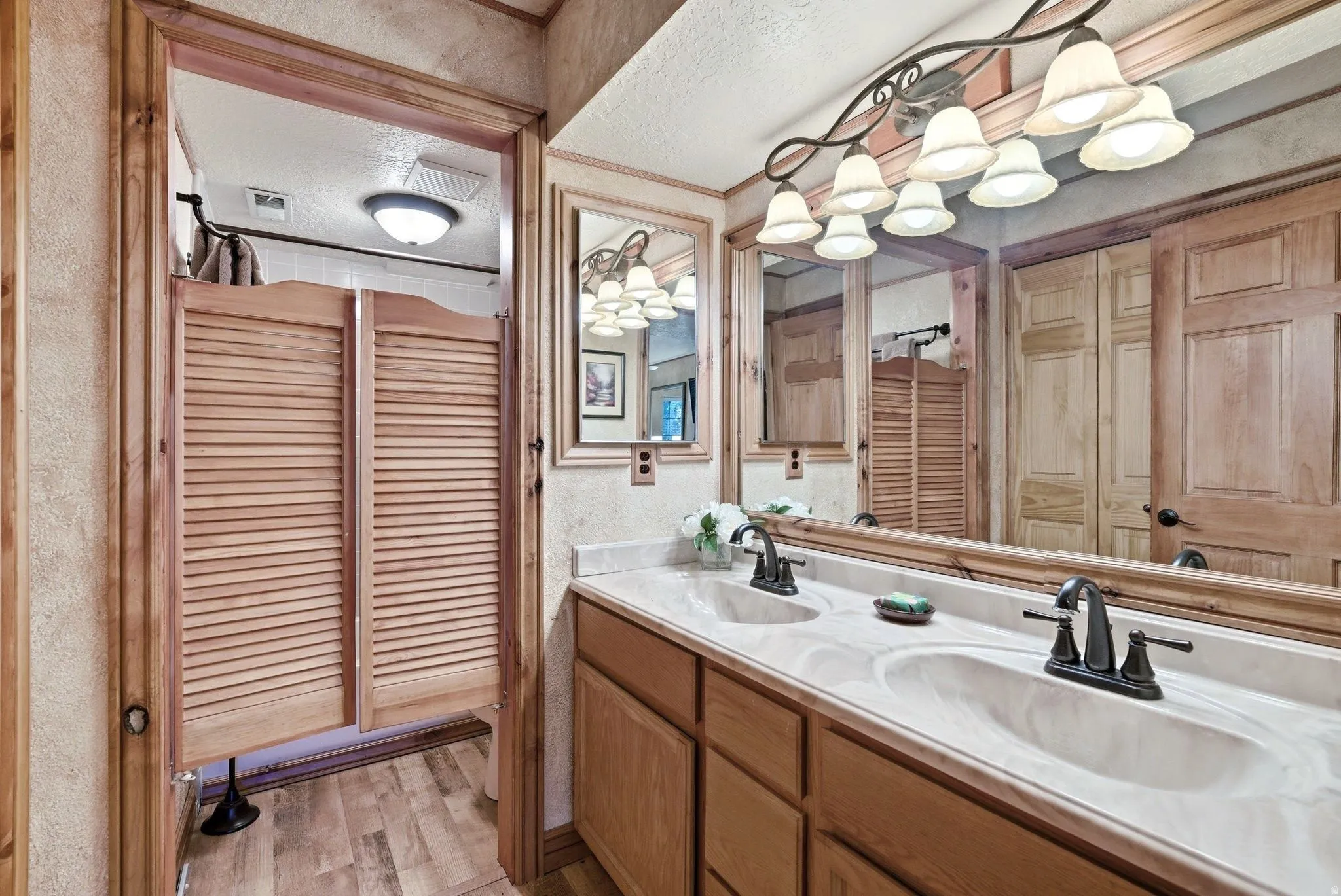 Bathroom vanity featuring a dual sink countertop with integrated sinks and dark bronze-finish faucets, a large wall-mounted mirror, and a decorative eight-light fixture