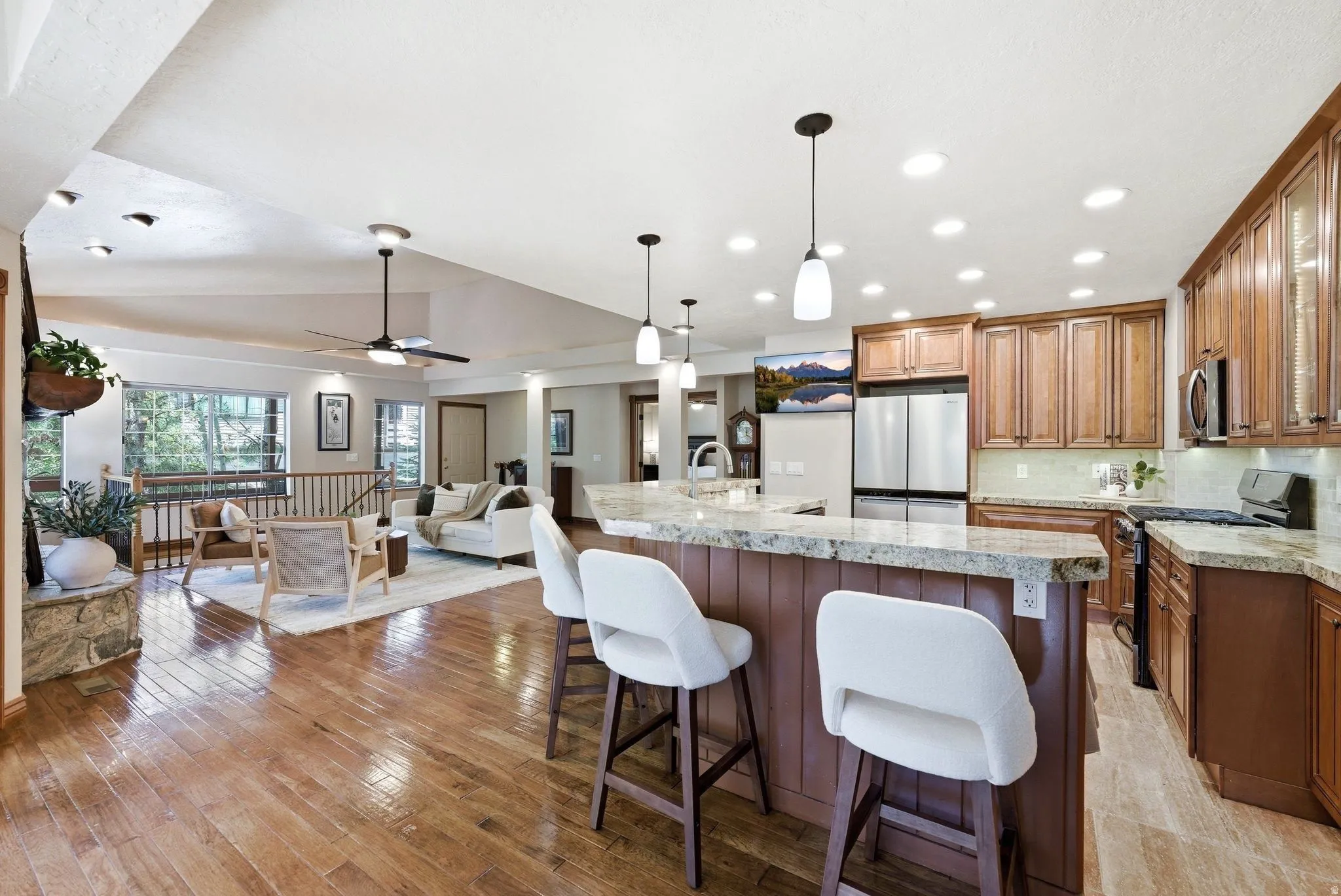 Open-concept living space featuring wood-finish flooring, a kitchen island with stone countertops, stainless steel appliances, recessed lighting, and a ceiling fan