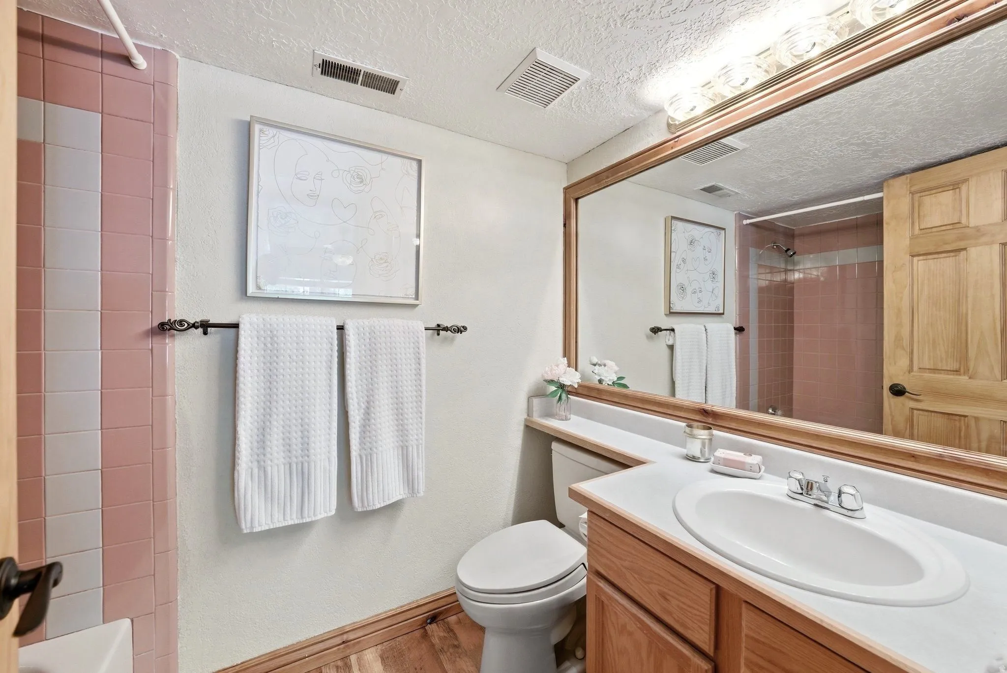 Bathroom featuring a wood-finish vanity with an integrated sink, a large wall-mounted mirror, and a tile shower surround with pink and white square tiles