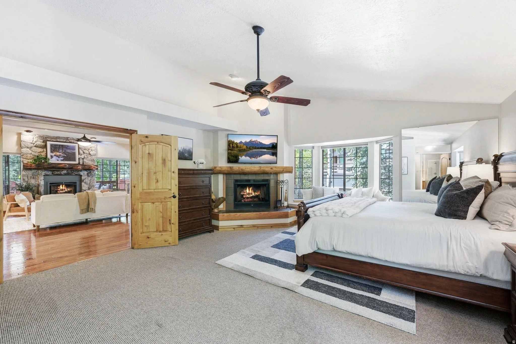 Carpeted bedroom featuring a vaulted ceiling and a corner fireplace with a timber mantel