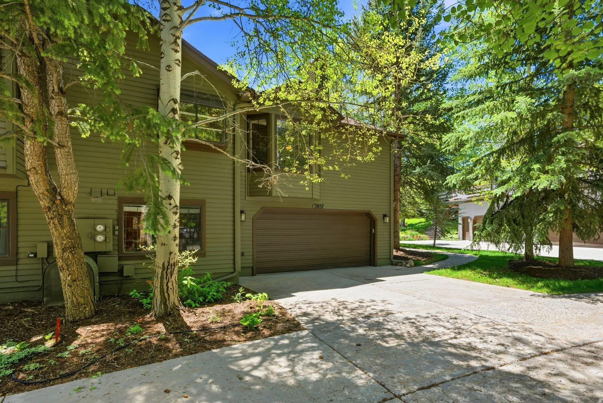 Exterior featuring horizontal siding, an integrated garage, a concrete driveway, established trees, and surrounding greenery