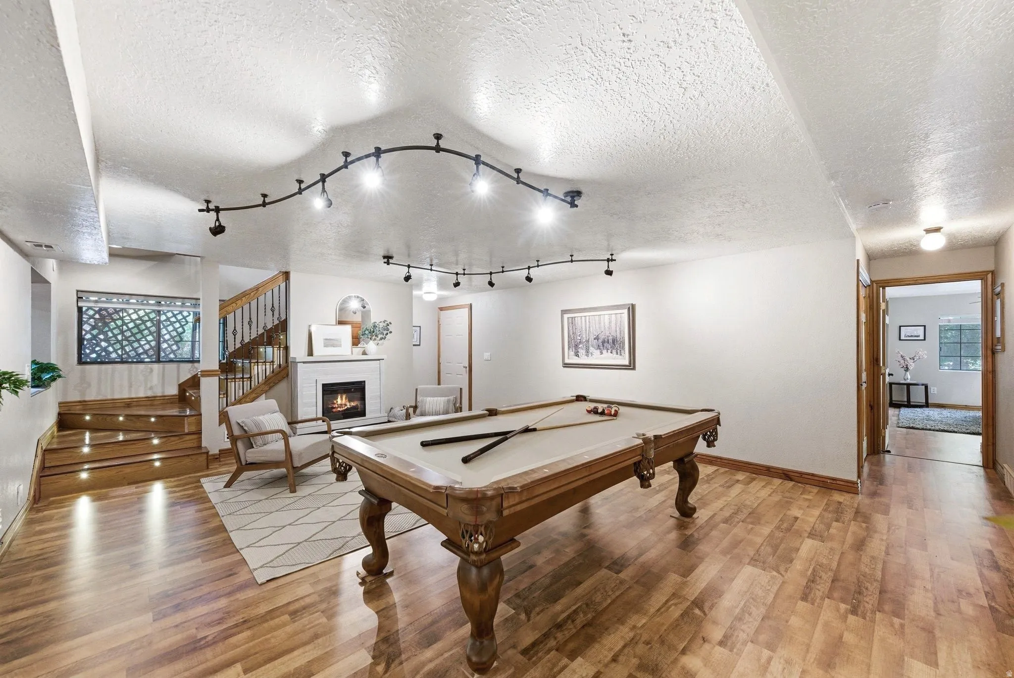 Versatile entertainment space featuring wood-finish flooring, a fireplace with a white surround, and track lighting