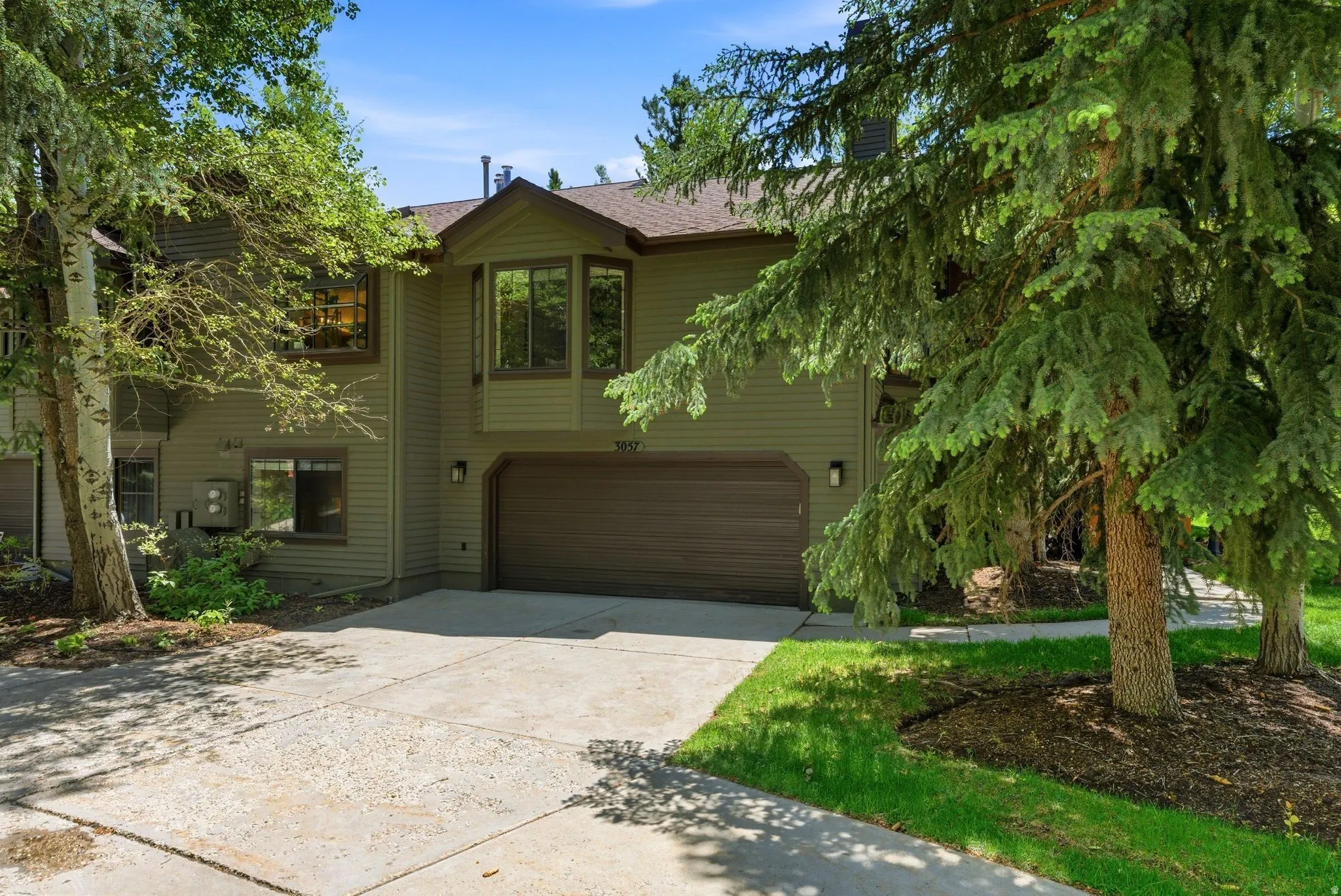 Two-story exterior with horizontal siding, an integrated garage, a bay window, and mature trees