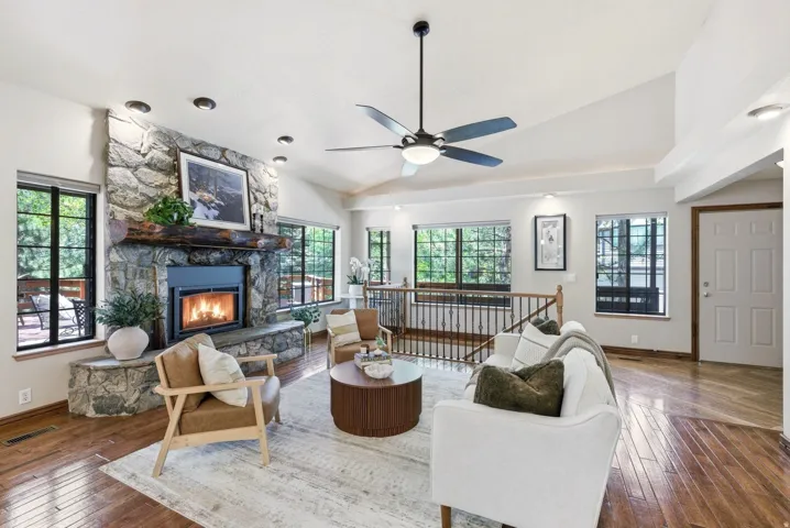 Spacious living area featuring a stone-clad fireplace with wood mantel, vaulted ceilings, recessed lighting, and hardwood flooring