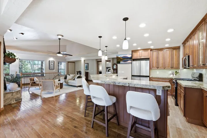Open-concept living space featuring wood-finish flooring, a kitchen island with stone countertops, stainless steel appliances, recessed lighting, and a ceiling fan