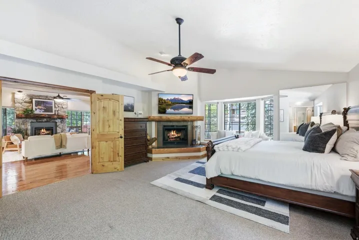 Carpeted bedroom featuring a vaulted ceiling and a corner fireplace with a timber mantel
