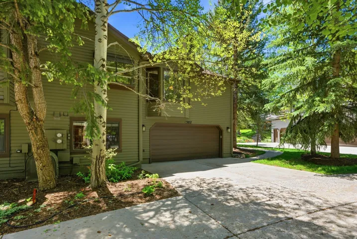 Exterior featuring horizontal siding, an integrated garage, a concrete driveway, established trees, and surrounding greenery