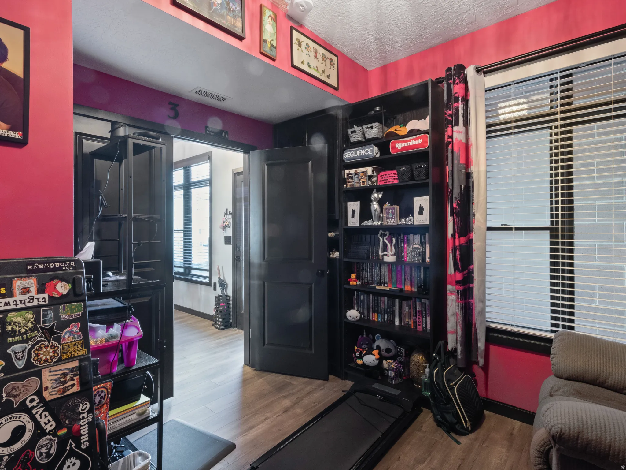 Room featuring wood-finish flooring, a built-in shelving unit, and a window with blinds