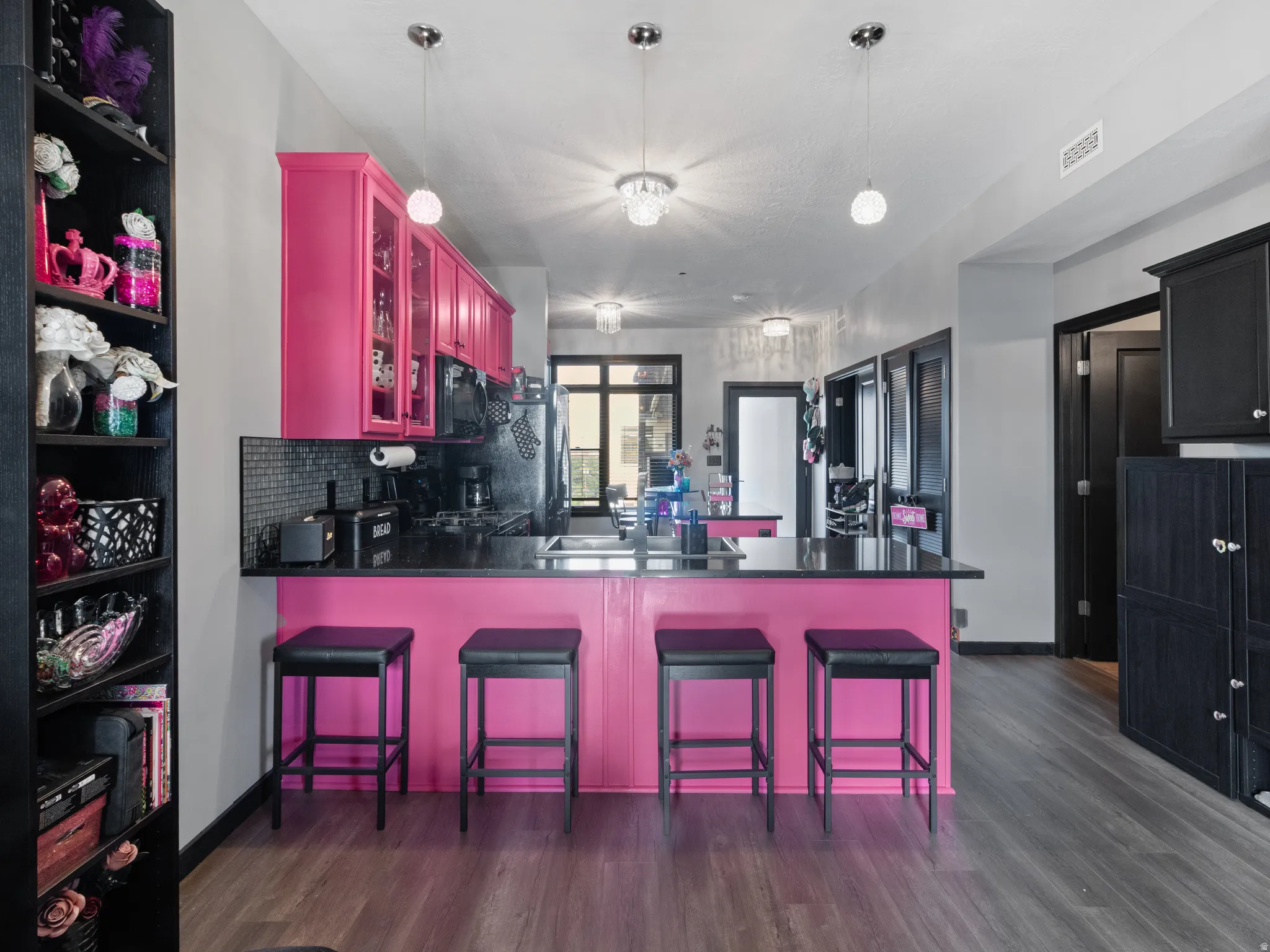 Kitchen featuring bright pink cabinetry, a breakfast bar with seating, black countertops, and a subway tile backsplash