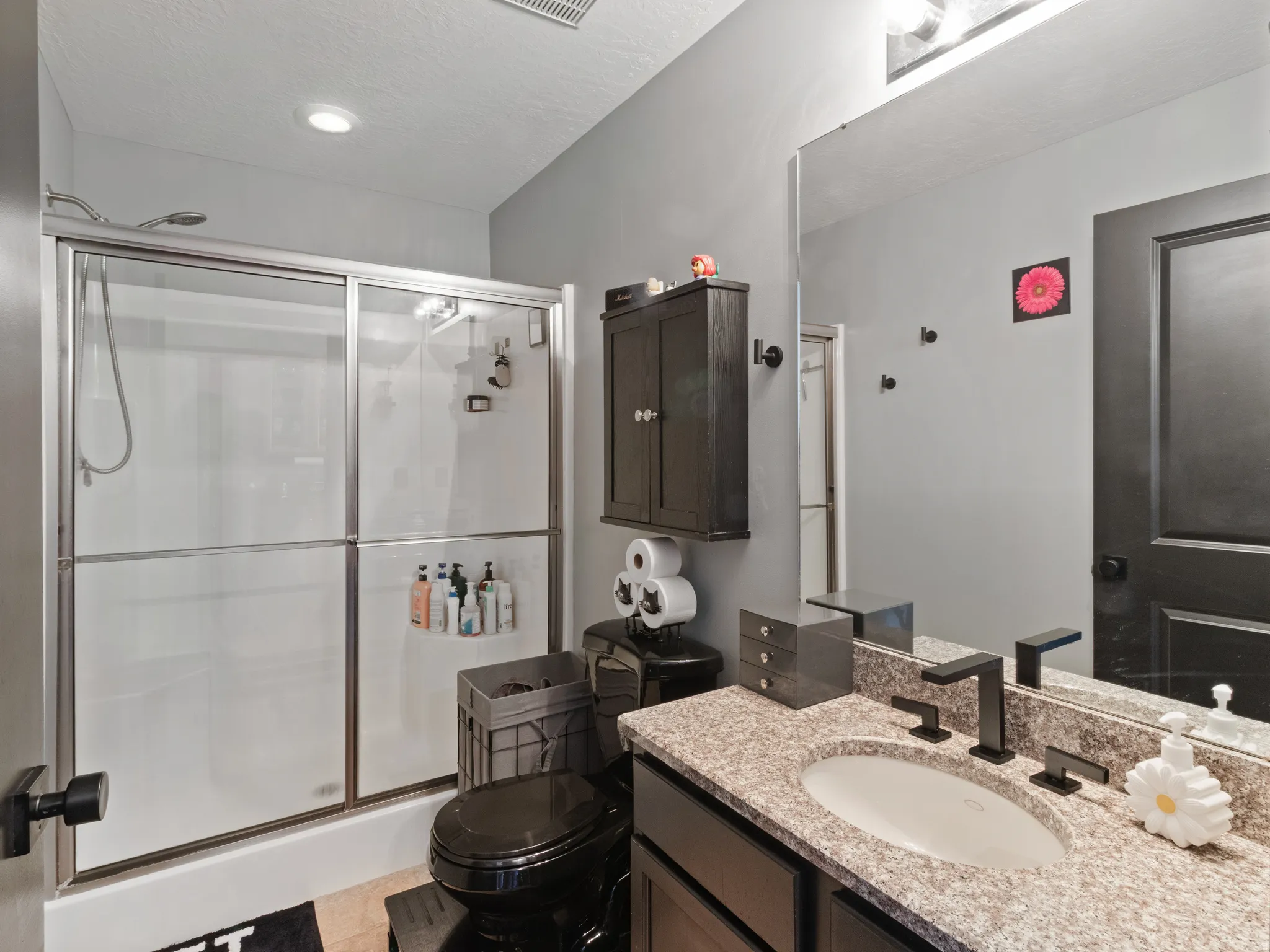 Bathroom featuring a shower with sliding glass doors, a granite-finish countertop, an undermount sink, a matte black faucet, and dark wood-finish cabinetry