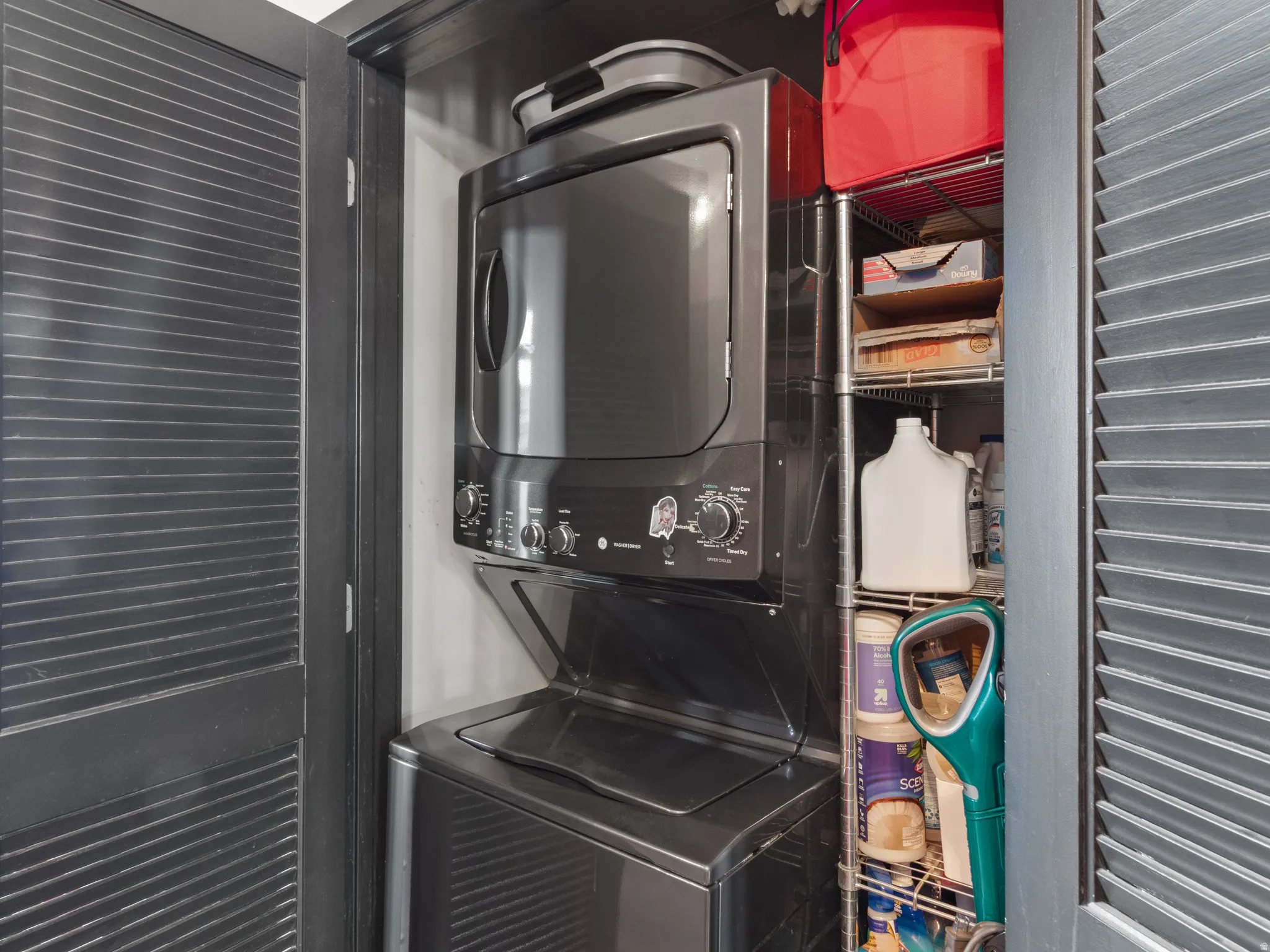 Stackable washer and dryer unit with dark finish, situated within a louvered bi-fold door enclosure