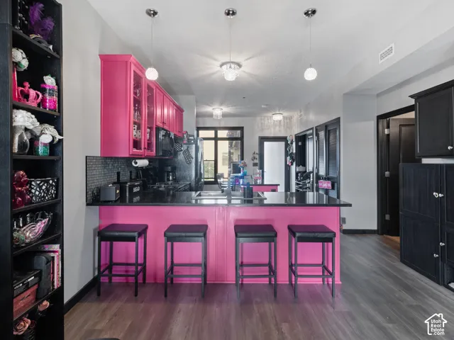 Kitchen featuring bright pink cabinetry, a breakfast bar with seating, black countertops, and a subway tile backsplash
