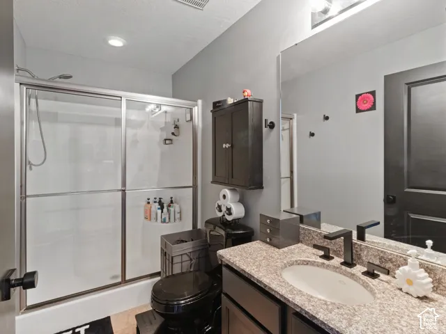 Bathroom featuring a shower with sliding glass doors, a granite-finish countertop, an undermount sink, a matte black faucet, and dark wood-finish cabinetry