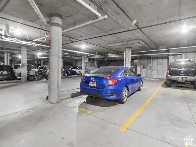 Concrete garage with overhead exposed piping, illuminated by multiple ceiling-mounted light fixtures