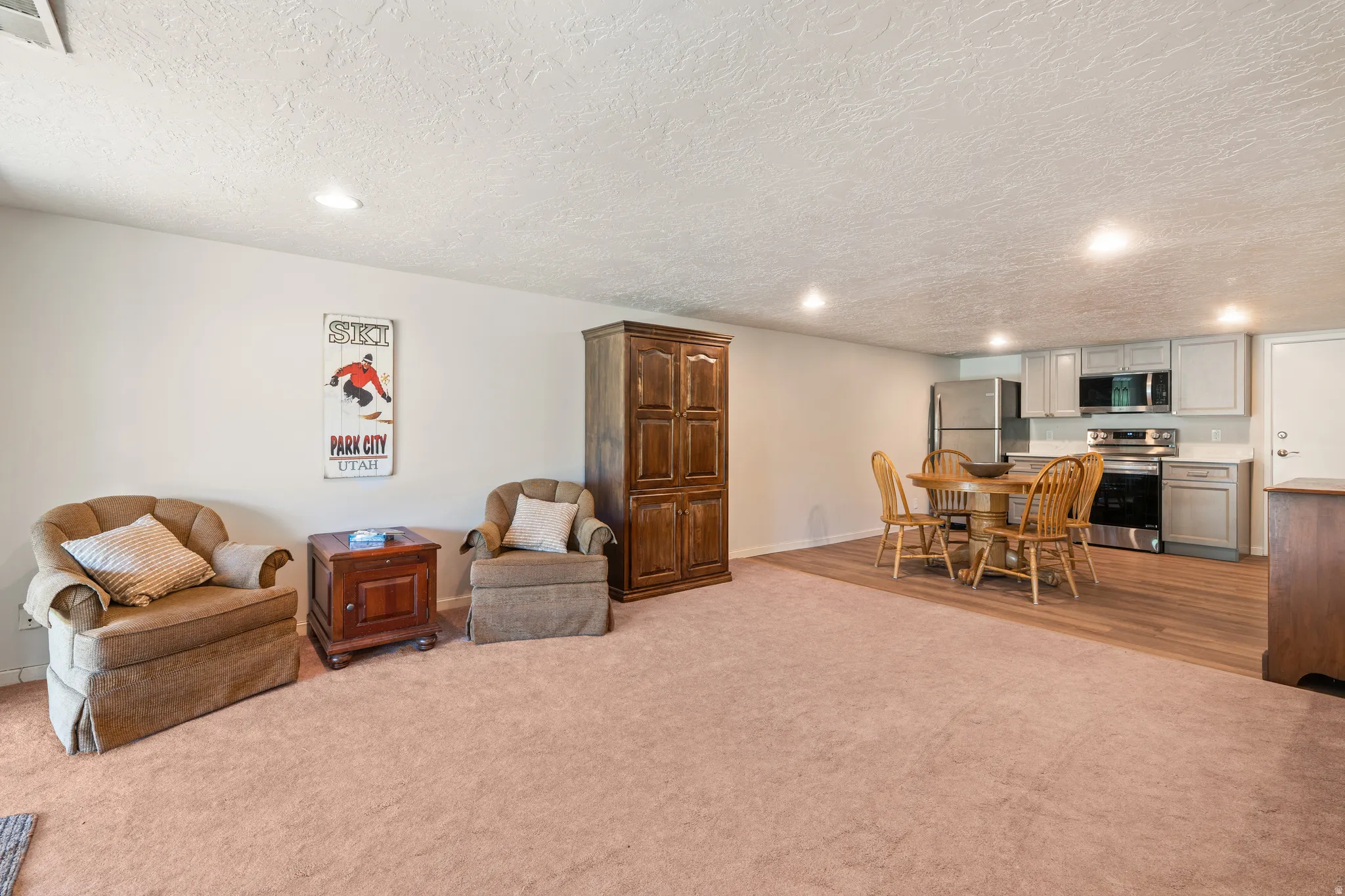 Open-concept living space featuring a full kitchen with stainless steel appliances, light gray cabinetry, and a subway tile backsplash