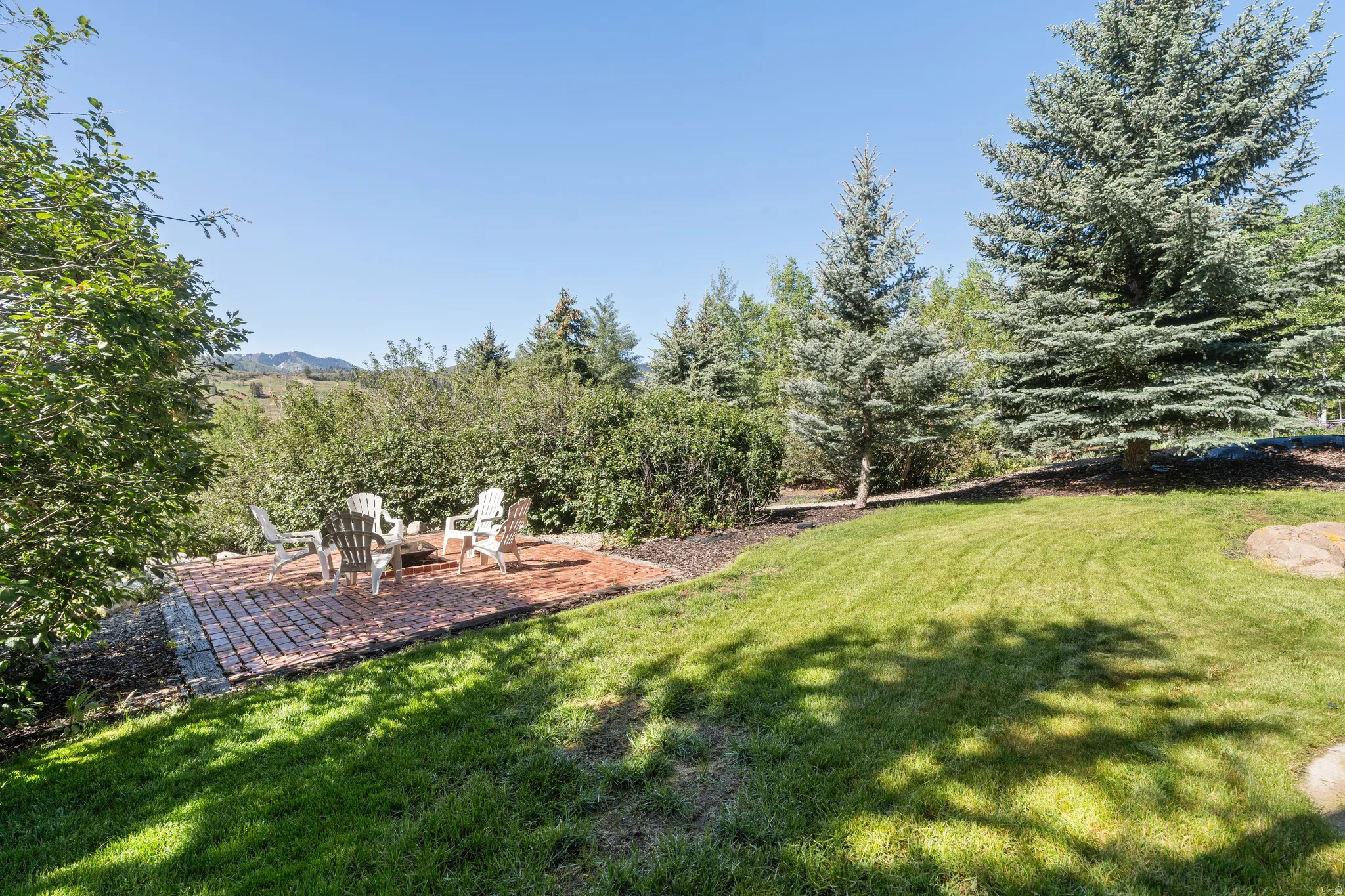 Outdoor patio featuring brick pavers, surrounded by mature trees and shrubs