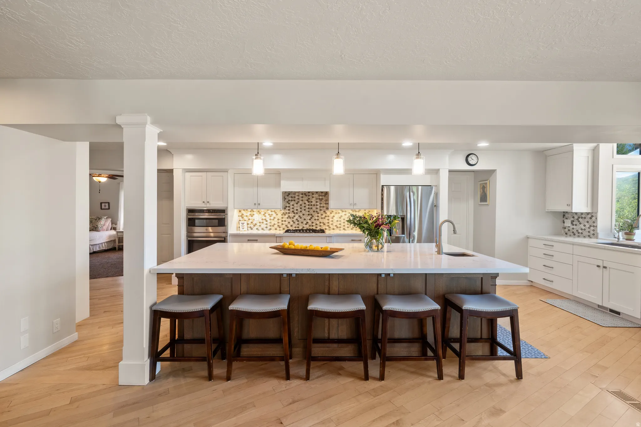 Spacious kitchen featuring a large central island with seating, white shaker cabinetry, stainless steel appliances, and wood-finish flooring