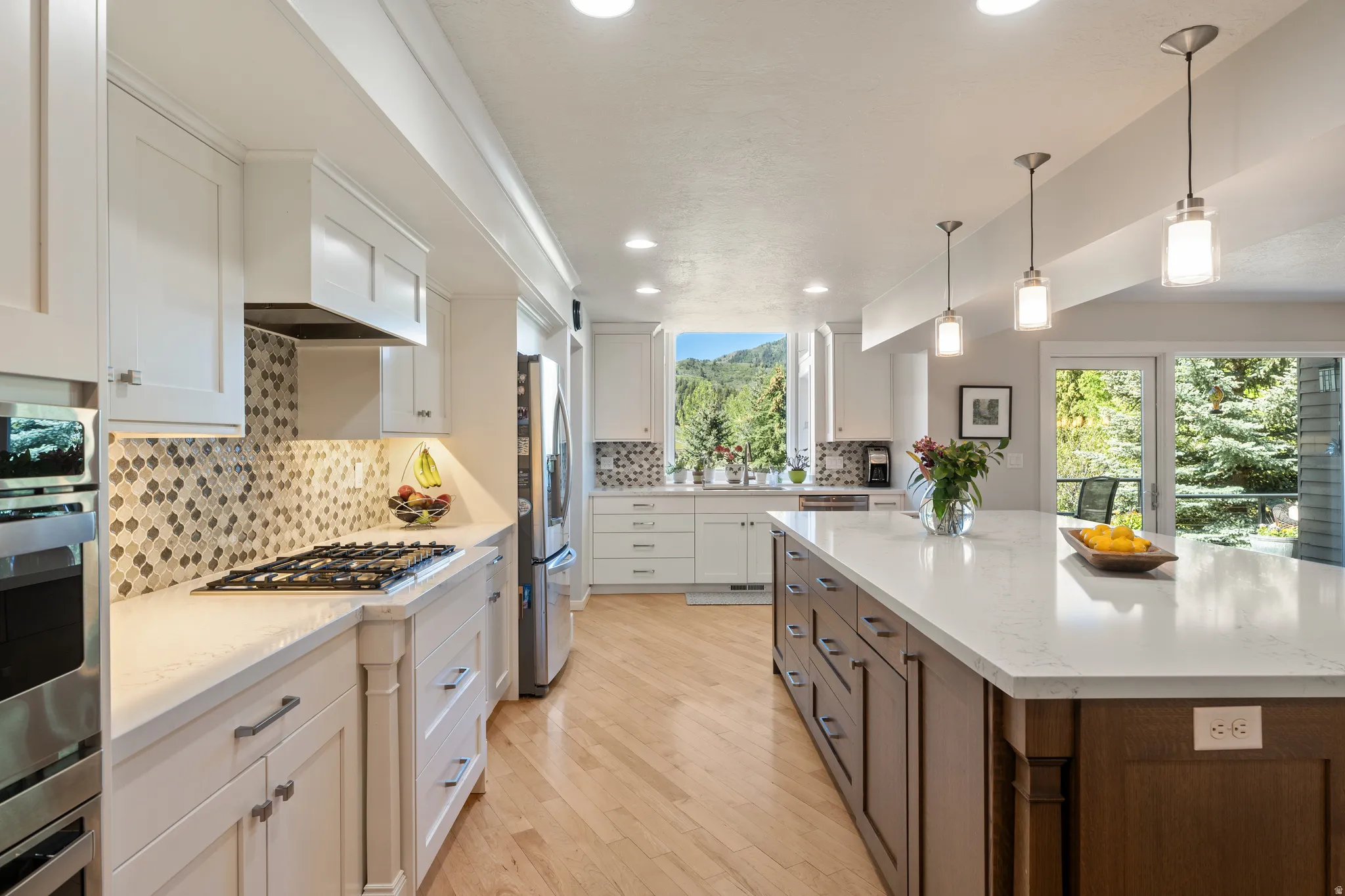 Kitchen featuring a large central island with a light countertop, wood-finish flooring, white cabinetry, integrated stainless steel appliances, and a mosaic tile backsplash