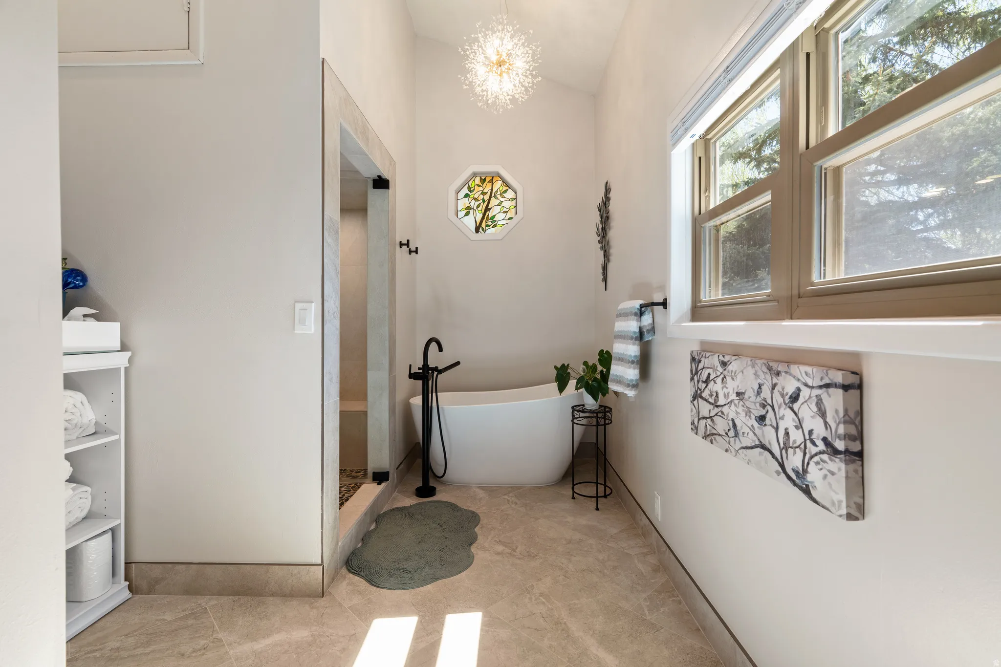 Spacious bathroom featuring a freestanding soaking tub with floor-mounted matte black faucet, a walk-in shower with glass enclosure, large window, vaulted ceiling, and tile flooring
