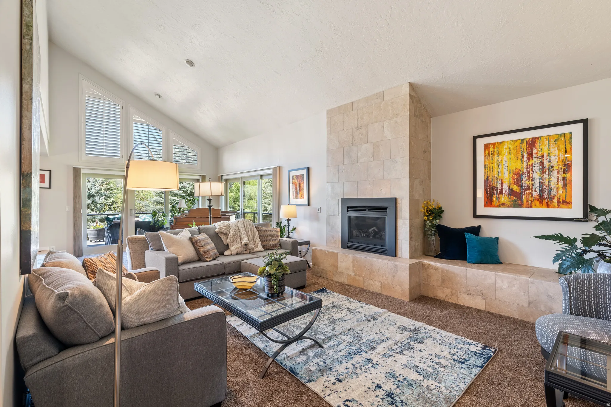 Vaulted ceiling living area featuring a stone-clad fireplace, integrated hearth seating, and large windows with plantation shutters