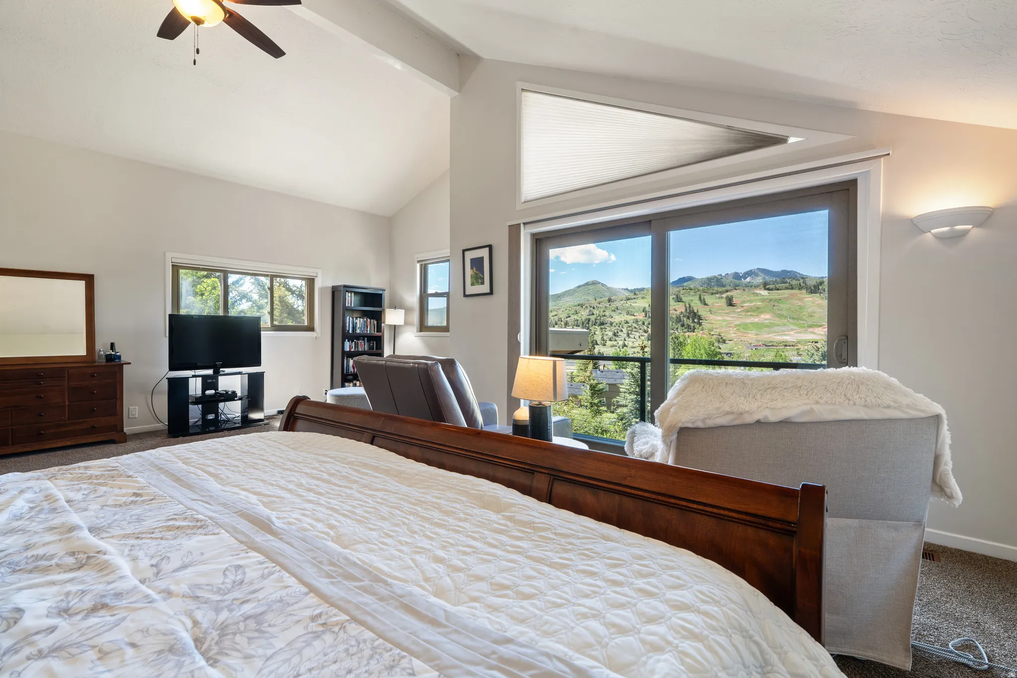 Vaulted ceilings featuring a ceiling fan, sliding glass doors to outdoor space, upper transom window, and expansive mountain scenery