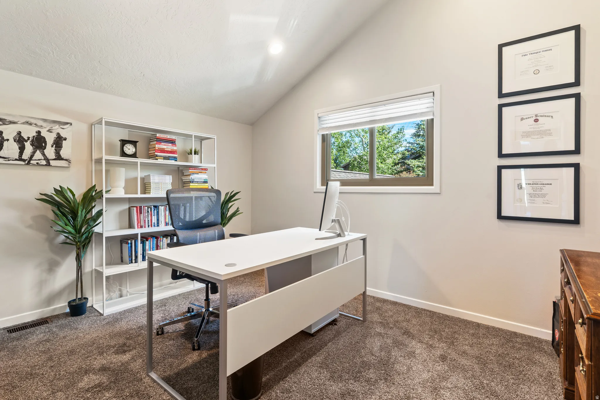 Dedicated office space featuring vaulted ceilings and a window providing exterior views
