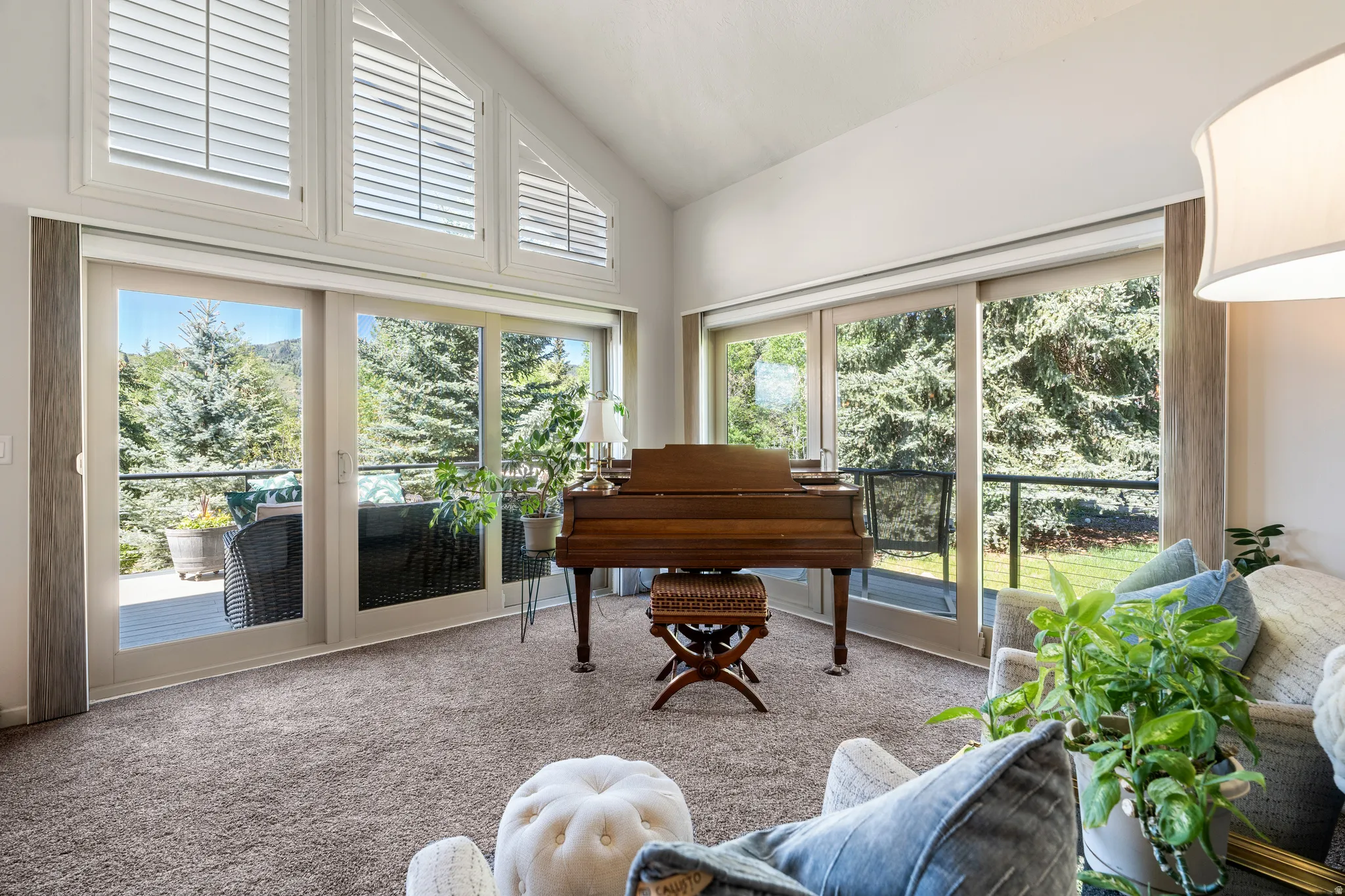 Vaulted ceiling living area featuring multiple glass sliding doors, upper transom windows with plantation shutters, and soft gray carpeting