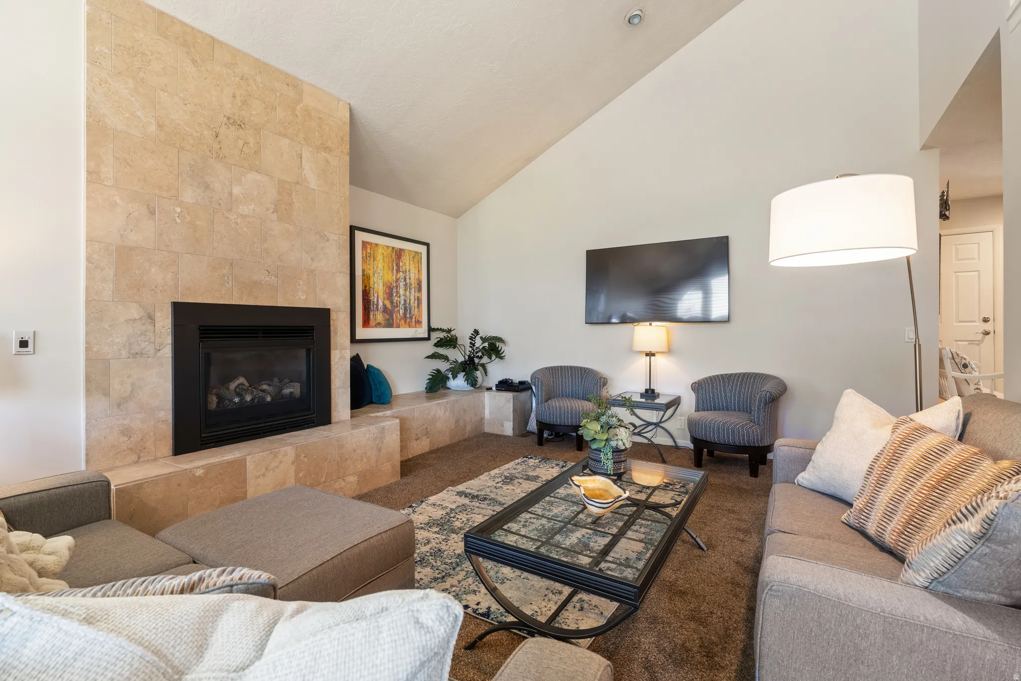 Living area featuring a stone-clad fireplace with a black hearth, vaulted ceilings, and recessed lighting