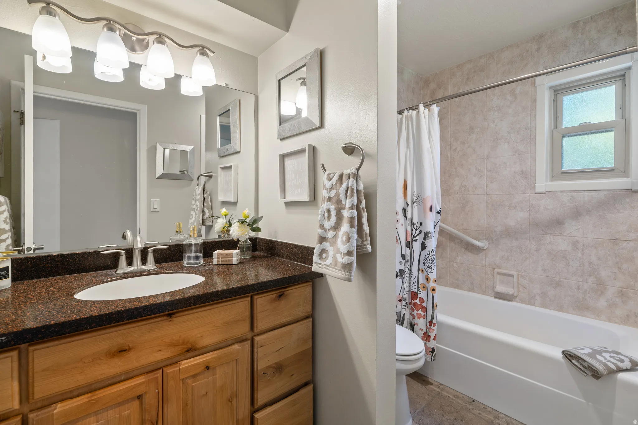 Bathroom featuring a natural wood vanity with a dark speckled countertop, an oval undermount sink, and a multi-bulb vanity light fixture