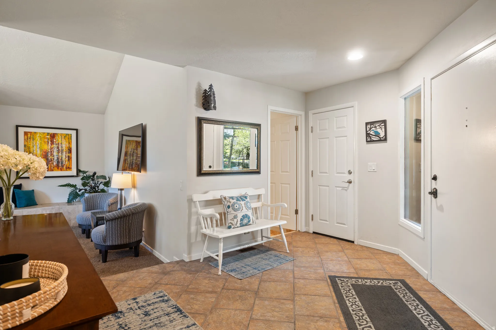 Inviting entryway featuring warm-toned tile flooring, a white panel door, and a full-length sidelight