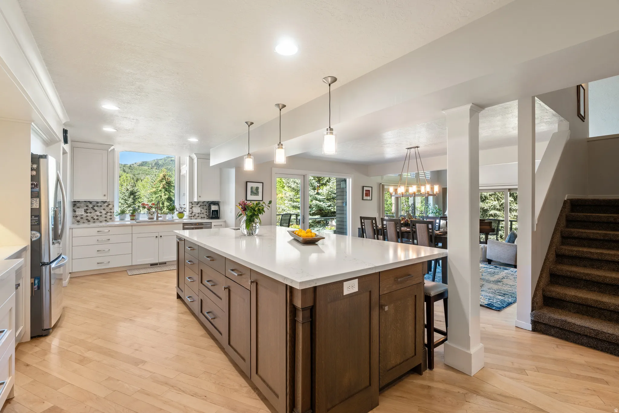 Spacious kitchen featuring a large central island with a light-toned countertop, light wood-finish flooring, white cabinetry, a tiled backsplash, and recessed lighting