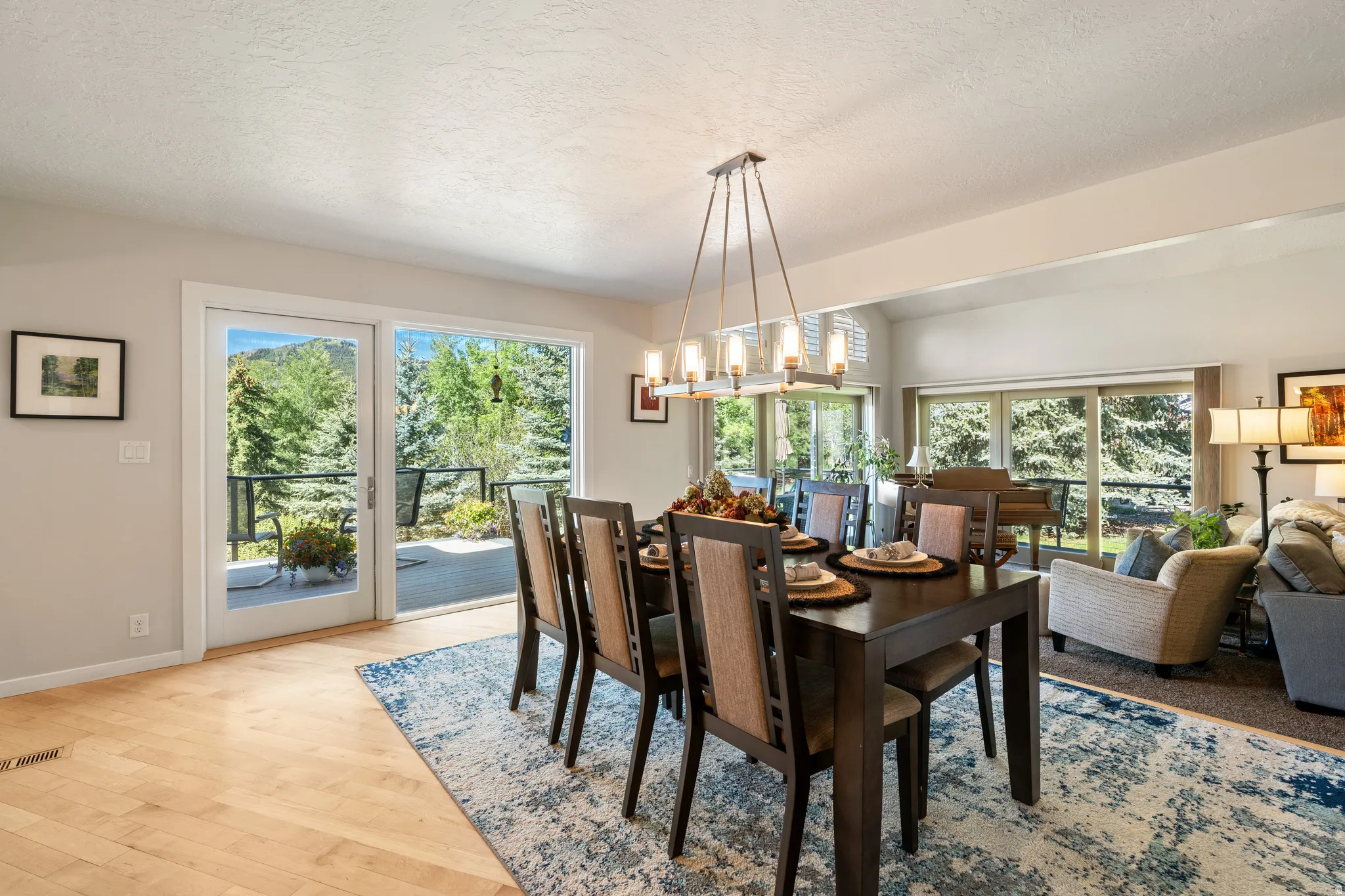 Open-concept dining area featuring light wood-finish flooring, a contemporary linear chandelier, and sliding glass doors that open to an outdoor deck