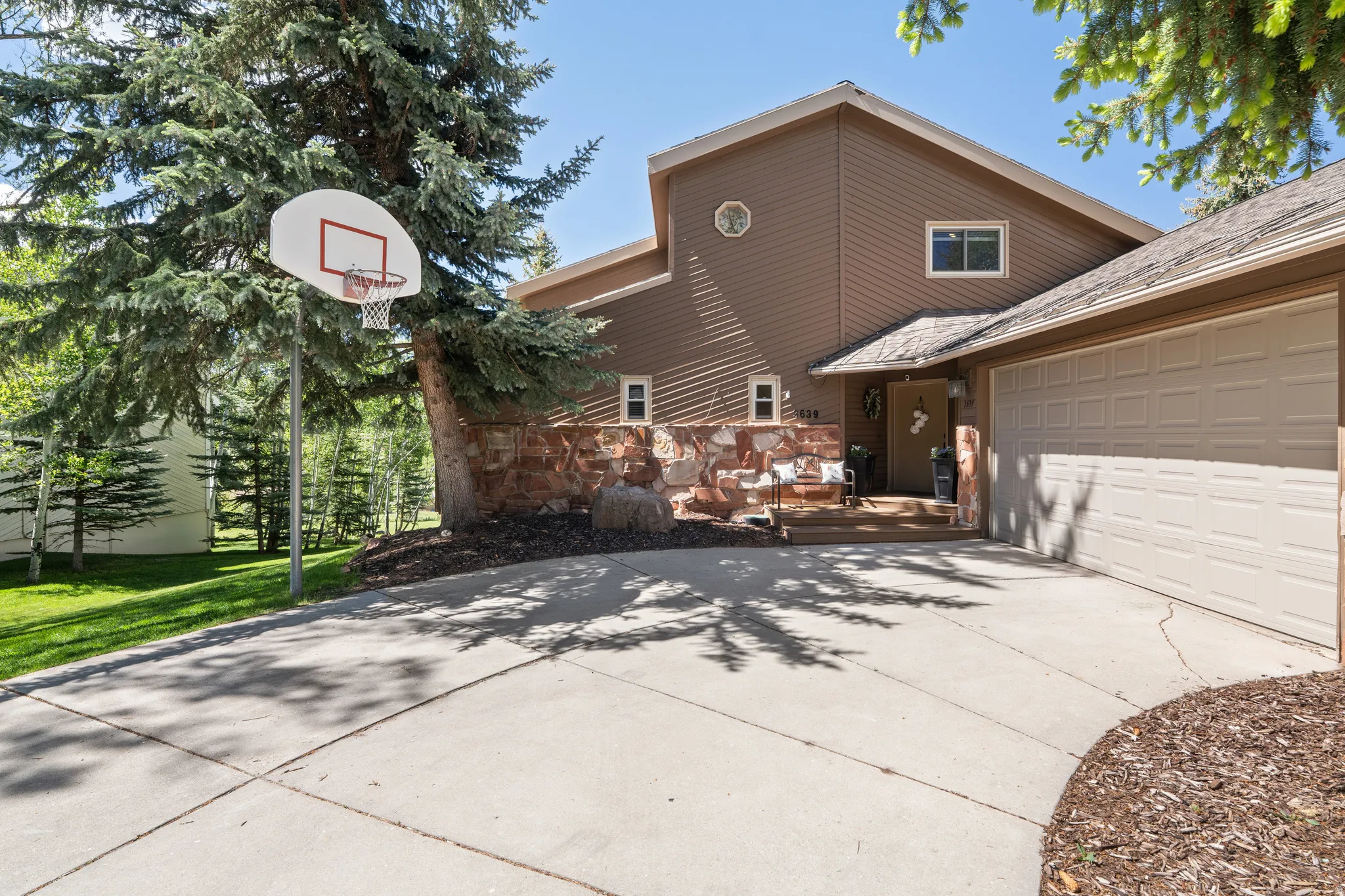 Exterior featuring a concrete driveway, attached garage, stone accents, and mature evergreen trees