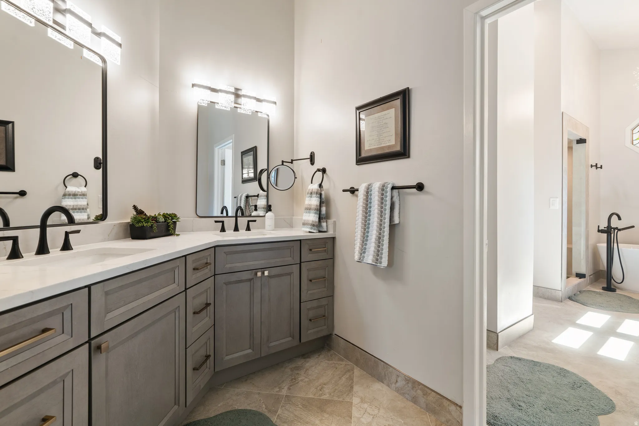 Bathroom featuring a dual vanity with gray shaker-style cabinetry, white countertops, and matte black hardware