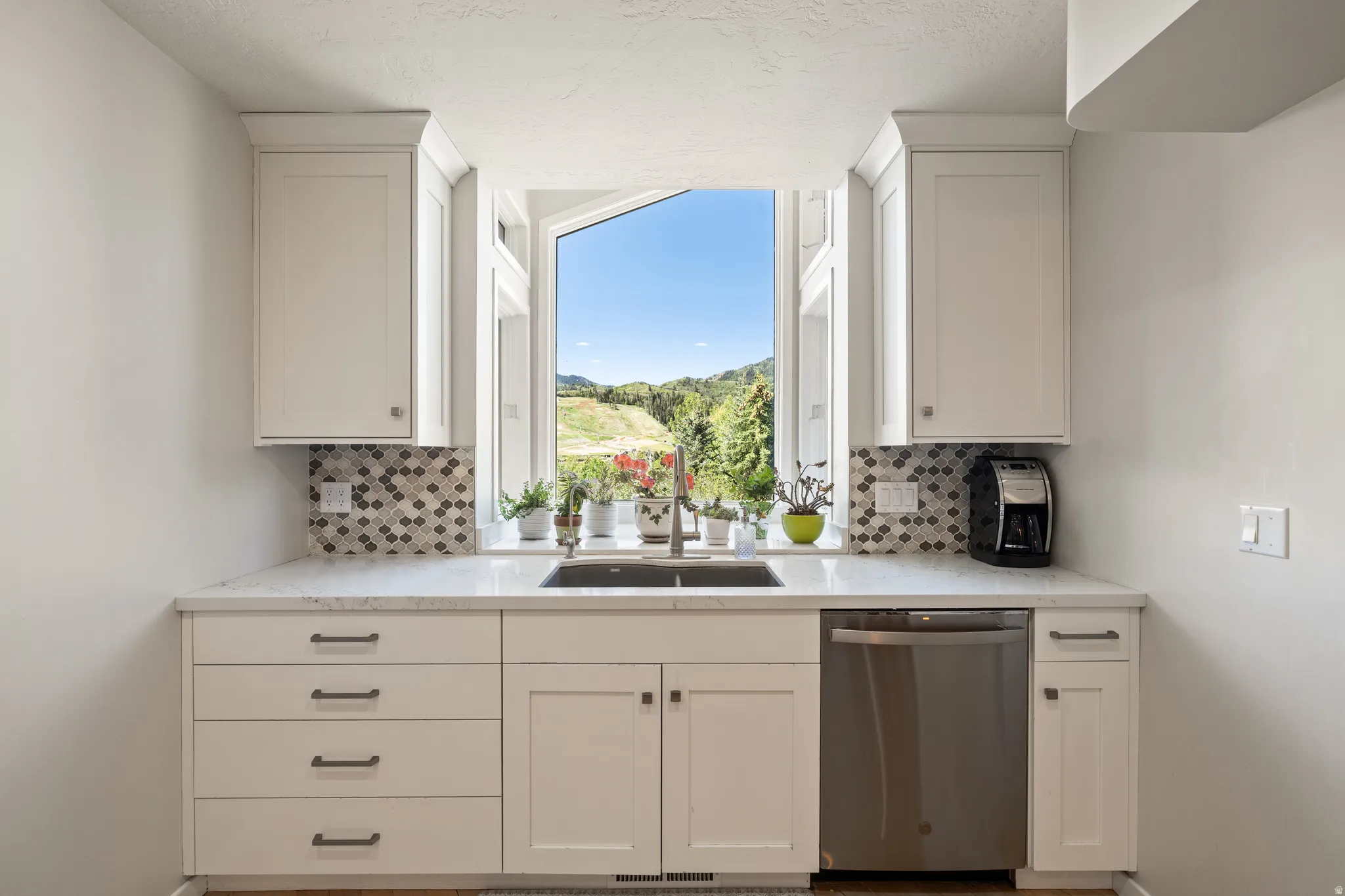 Kitchen workstation with white cabinetry, stainless steel sink, and stainless steel dishwasher