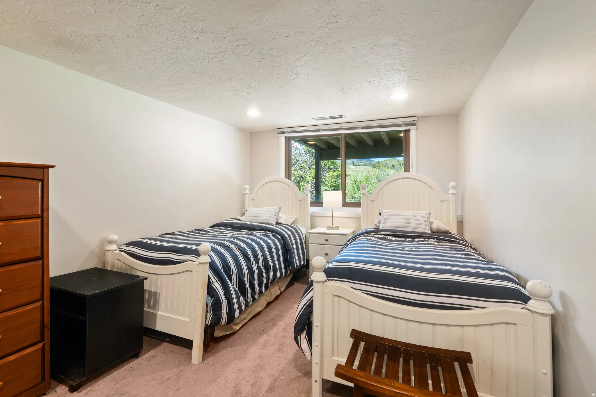 Bedroom featuring two white beadboard beds, a window with exterior green landscaping, recessed lighting, and textured ceiling